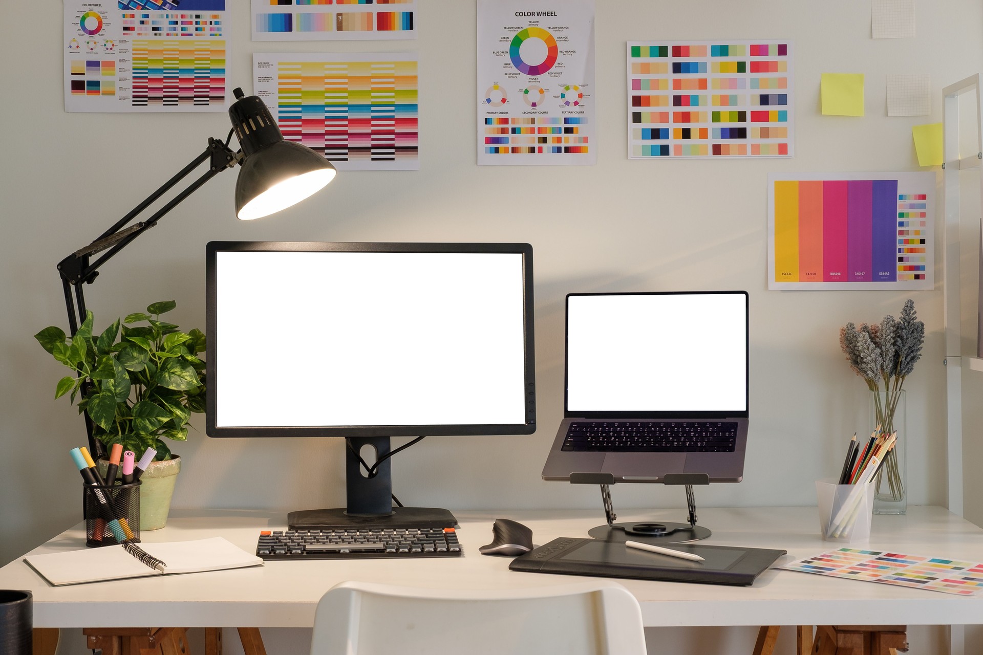 Modern graphic designer workspace with blank monitor and laptop screens , surrounded by color swatches, design tools.
